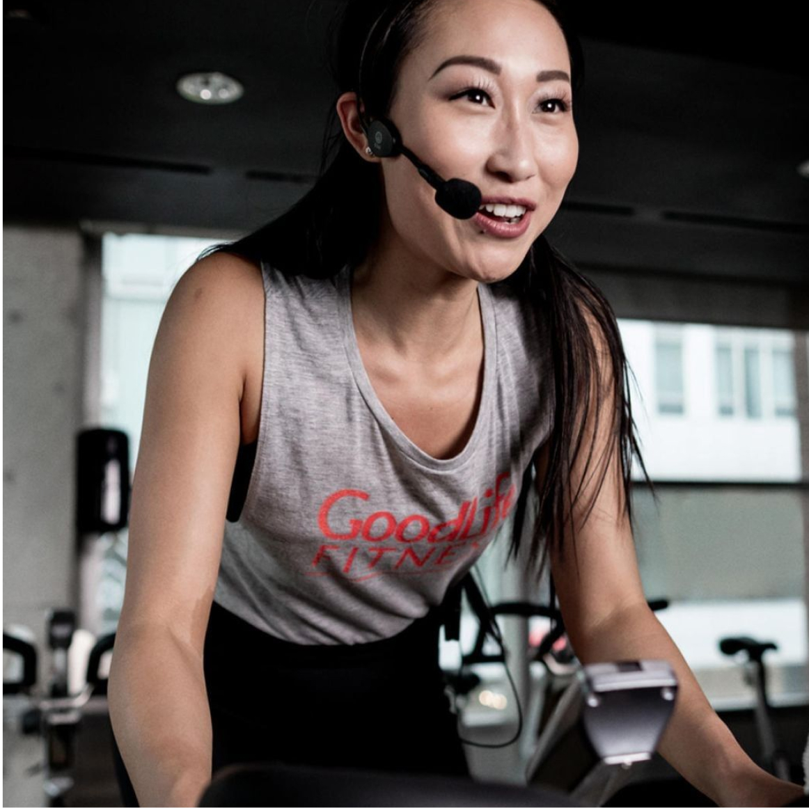 GoodLife Cycling class instructor on a stationary bike with a microphone headset 