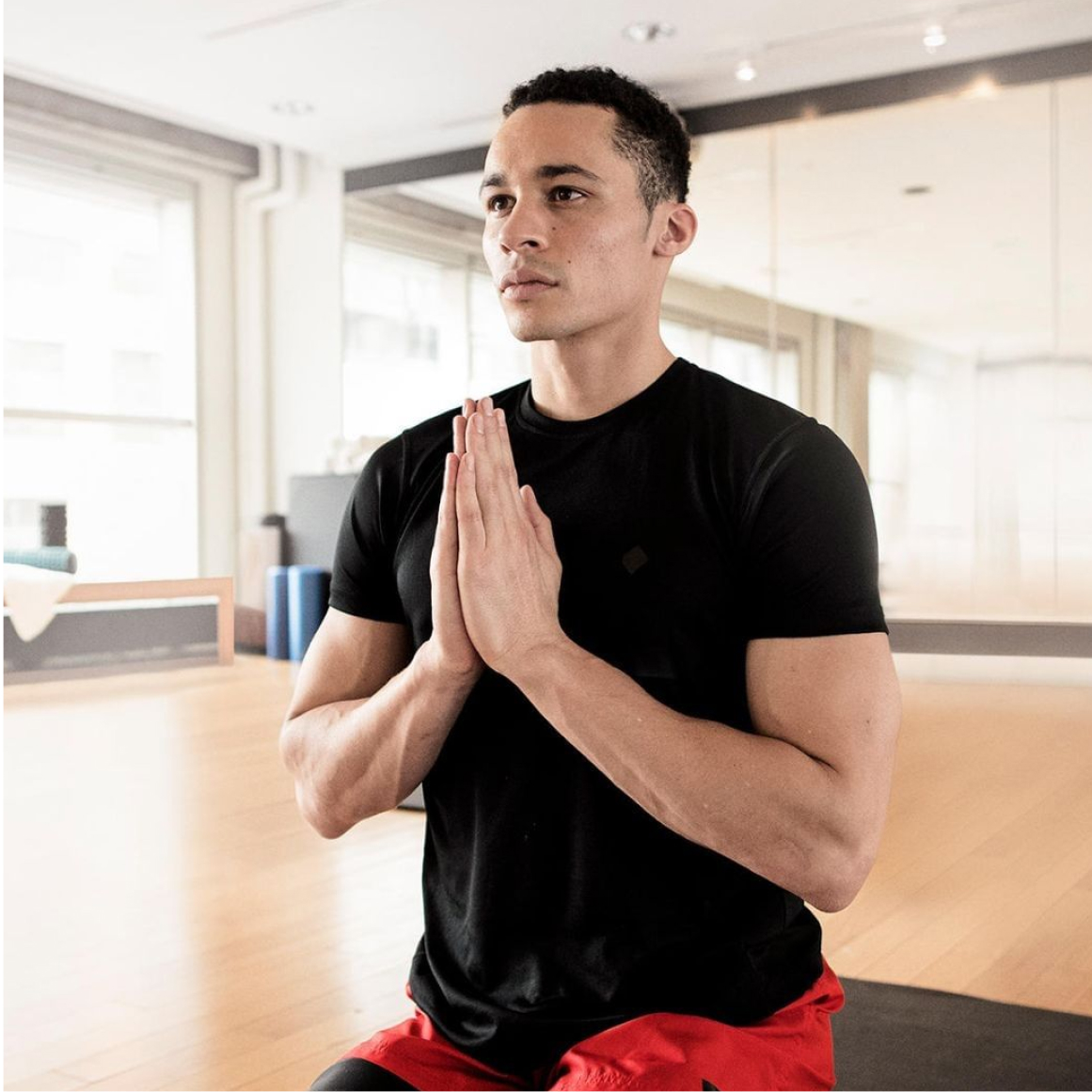 Man in black t-shirt sits on his knees with hands to heart centre