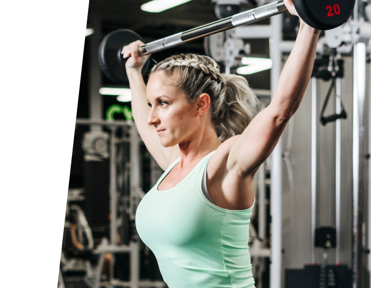 Woman in mint green tank top doing a barbell squat in weight area