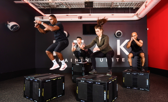 Four people doing box jumps onto black boxes in PEAK training space