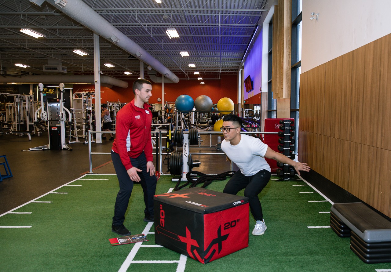 GoodLife Fitness trainer observes a client doing an exercise with medicine ball