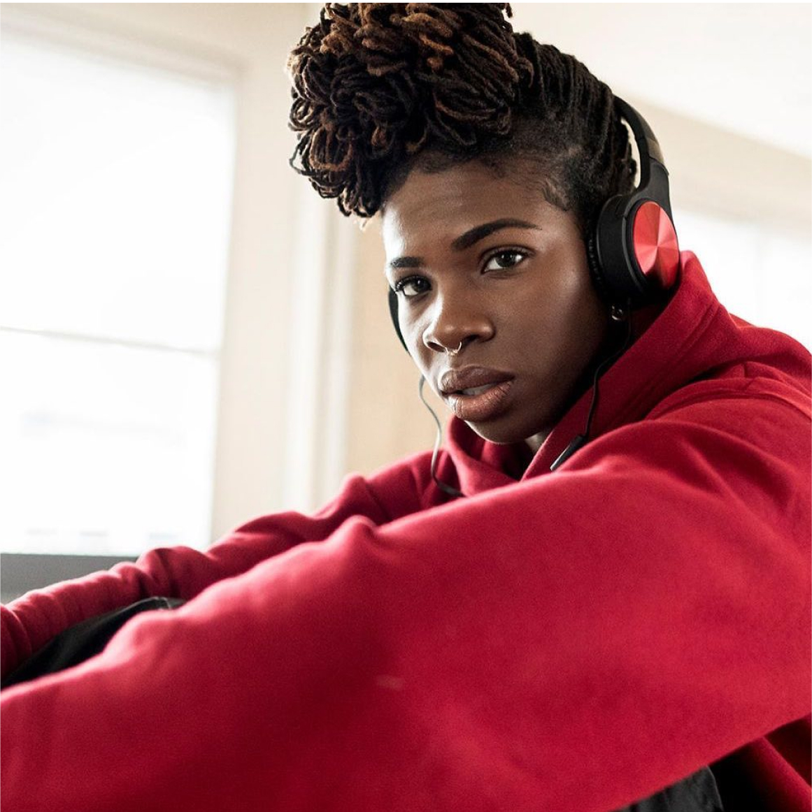 Woman in red sweatshirt with red and black on-ear headphones looks into the distance 