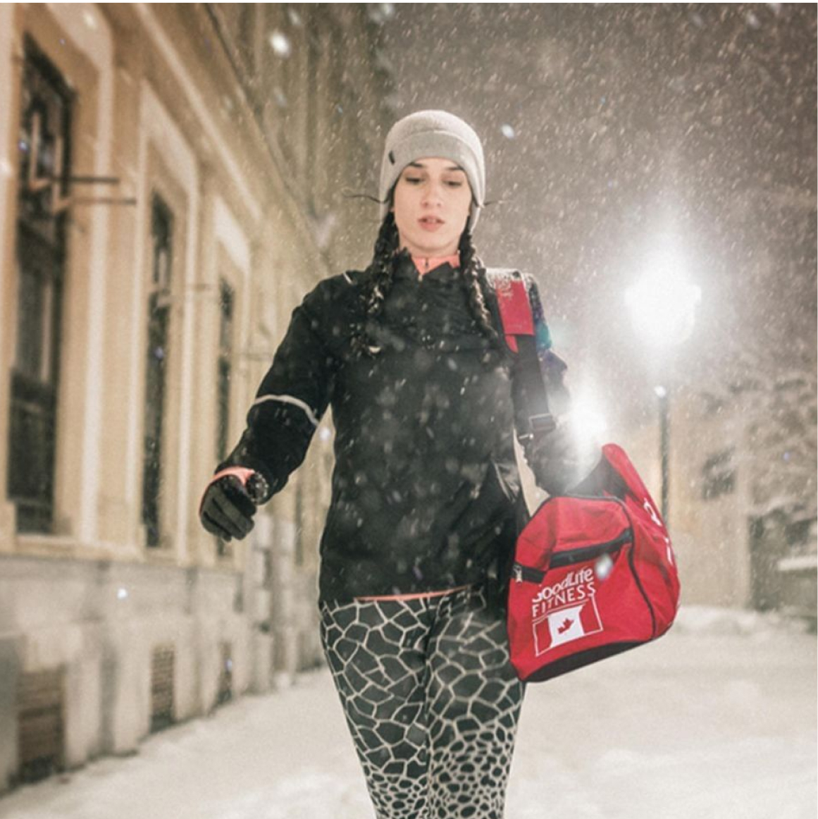 Woman walking in winter gear with red GoodLife Fitness gym bag