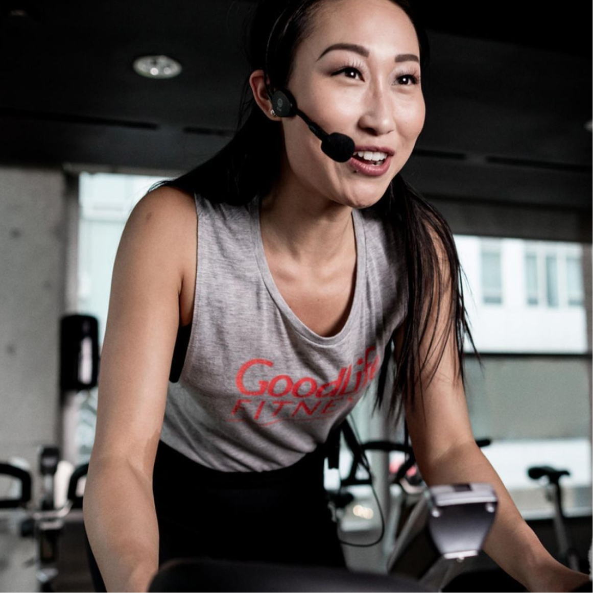 GoodLife Cycling class instructor on a stationary bike with a microphone headset 