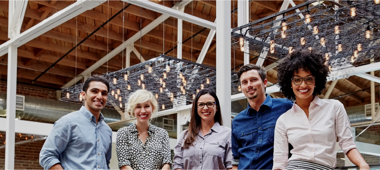 Group of five people in a workplace looking at camera and smiling