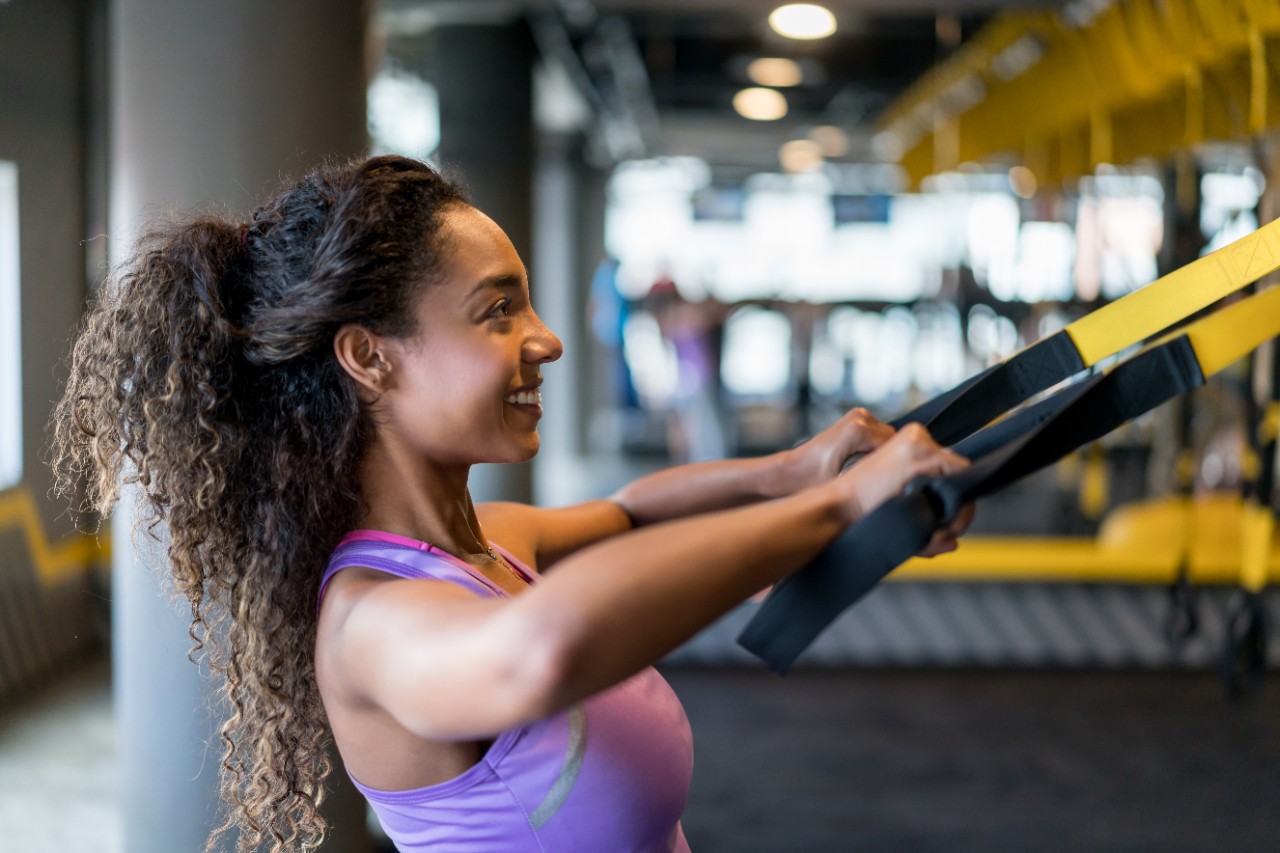 A young woman with a purple tank-top working out with TRX training bands.