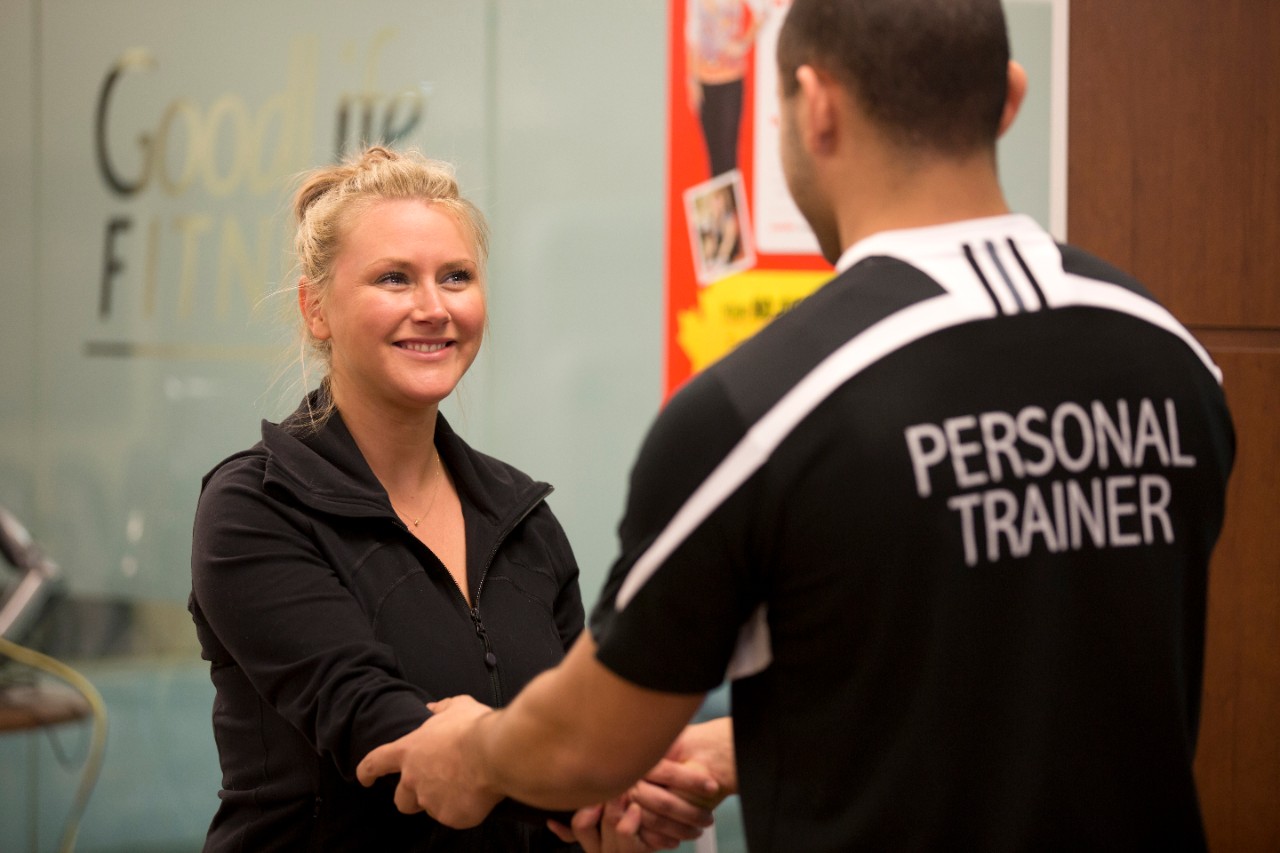 Male personal trainer shaking hands with a female client in a black, button-down shirt.