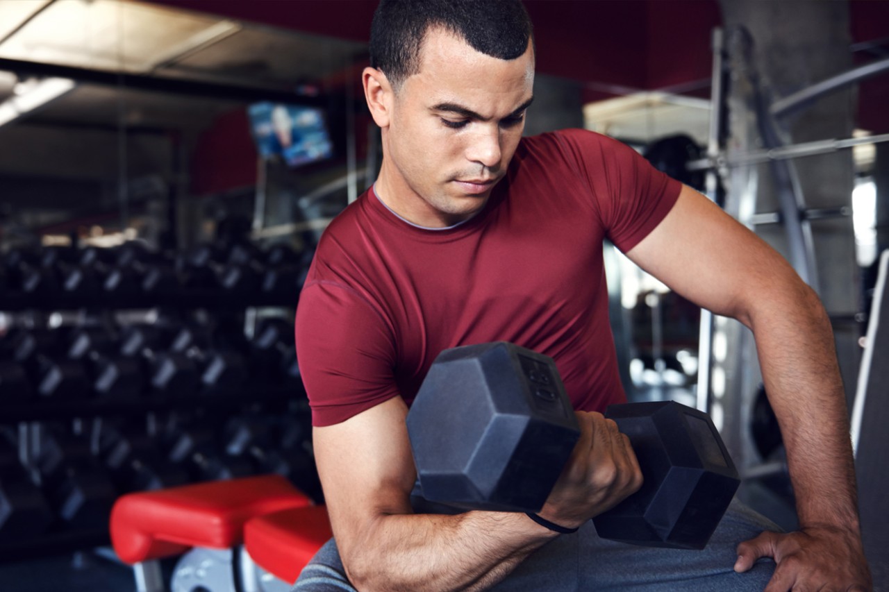 Man doing arm curls on a workout bench with a dumbbell.