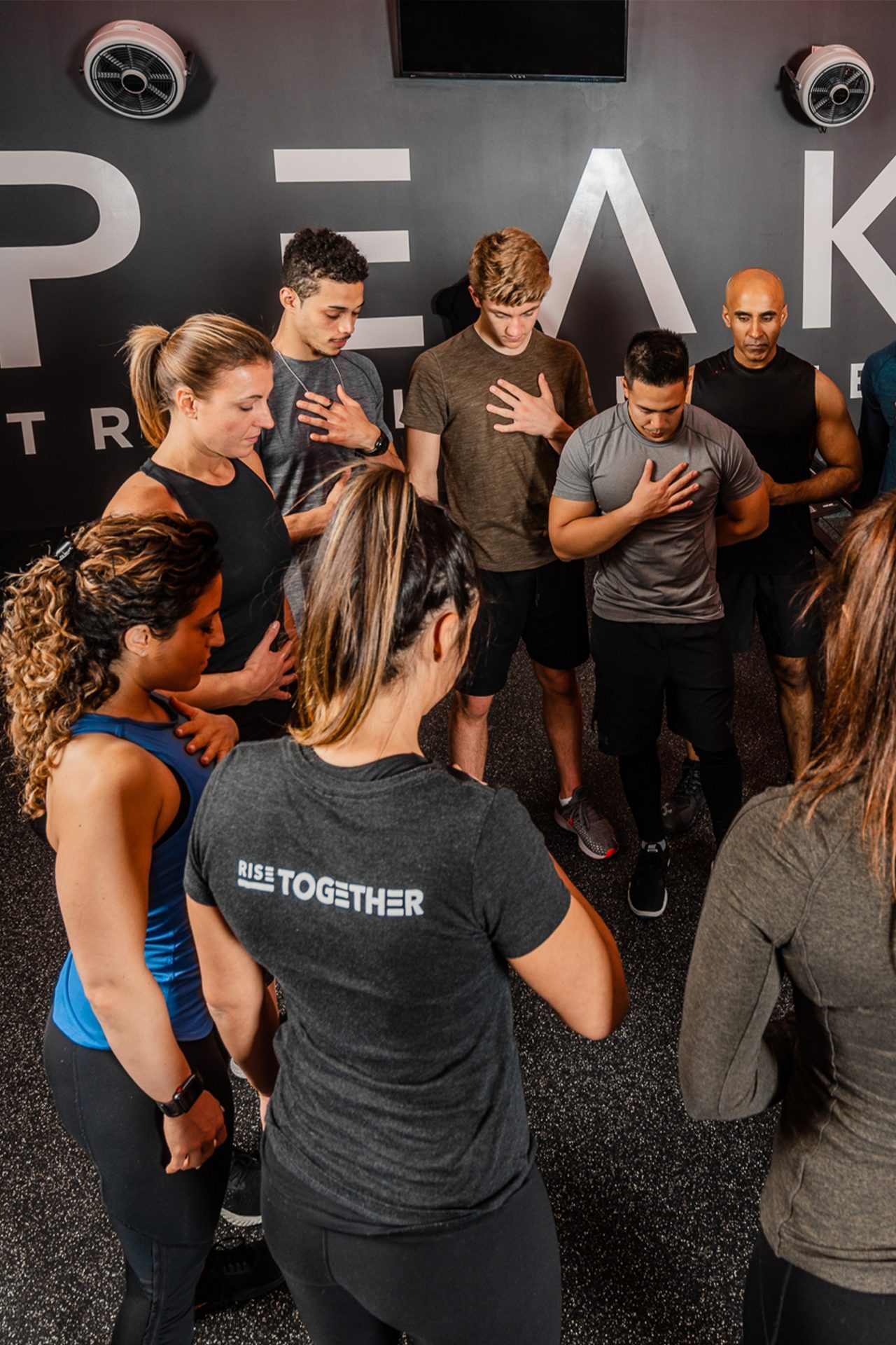 Group of men and women standing in a circle, with eyes closed and one hand on their chests