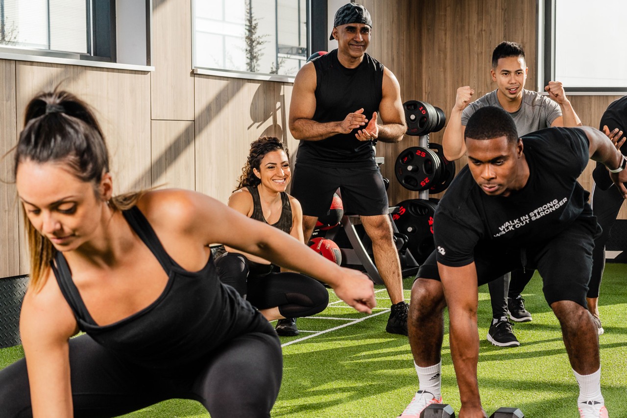 A group of men and women cheer on a man as he does a lunge