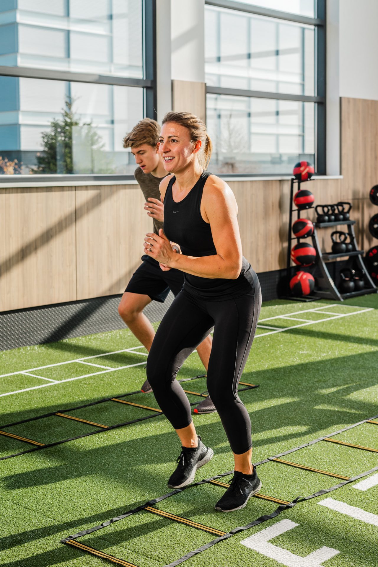 Woman and man perform agility ladder drills on turf