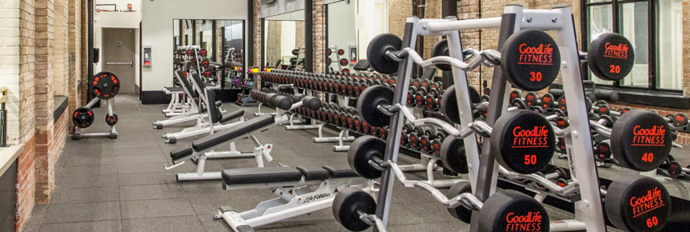 Weightlifting area in a GoodLife gym with barbells, dumbbells and lifting machines.