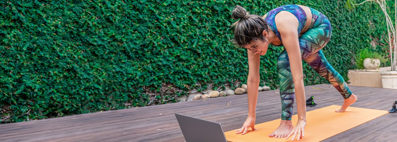 Woman lunging on a yoga mat watching a workout class on her laptop
